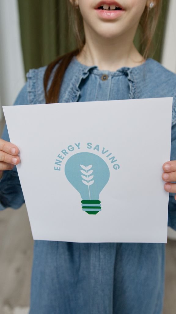 A Young Girl Holds A Sign Encouraging Energy Saving Efforts Indoors. 6990291 576x1024